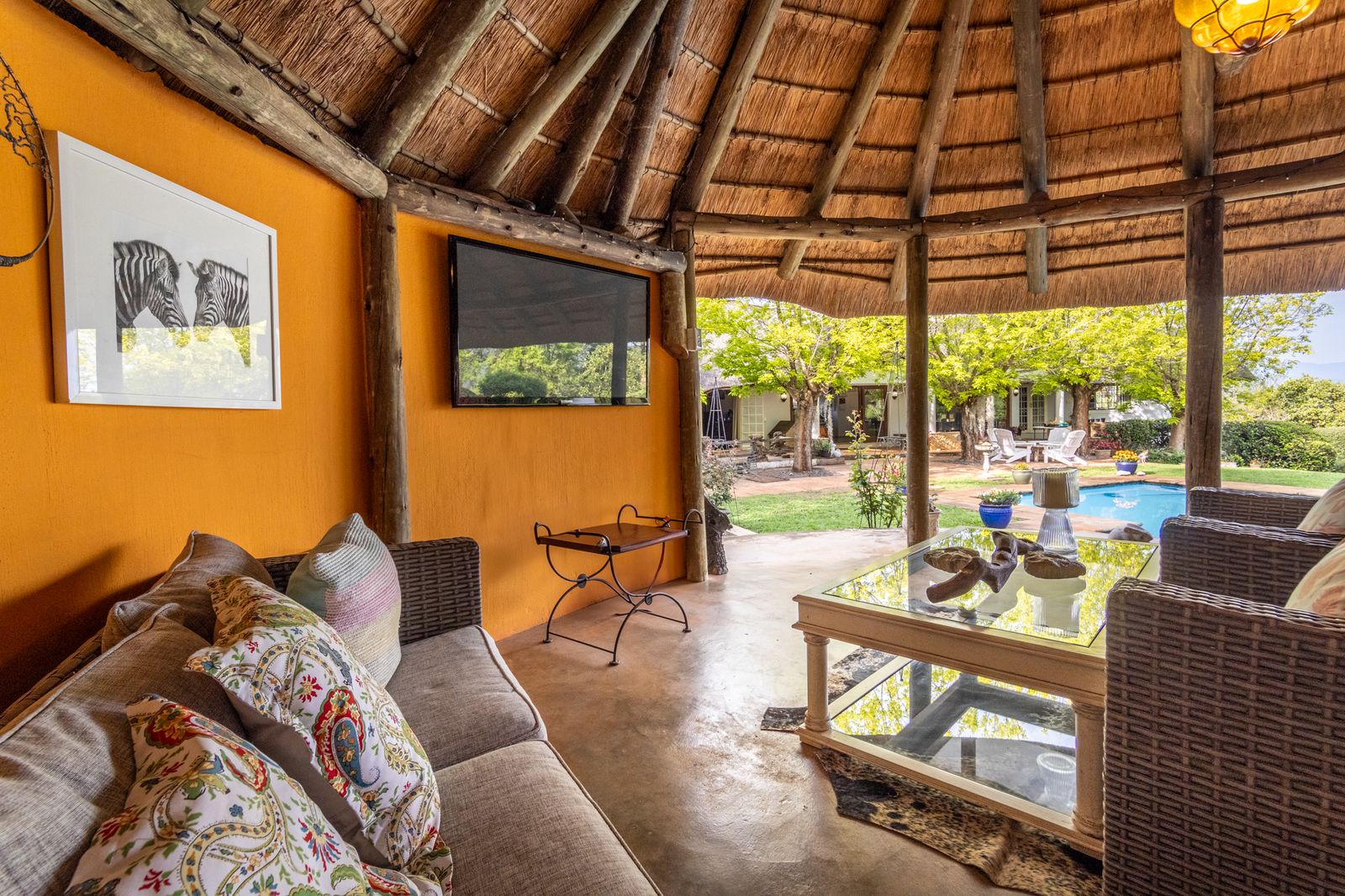 A thatched lounge opening onto a pool and garden