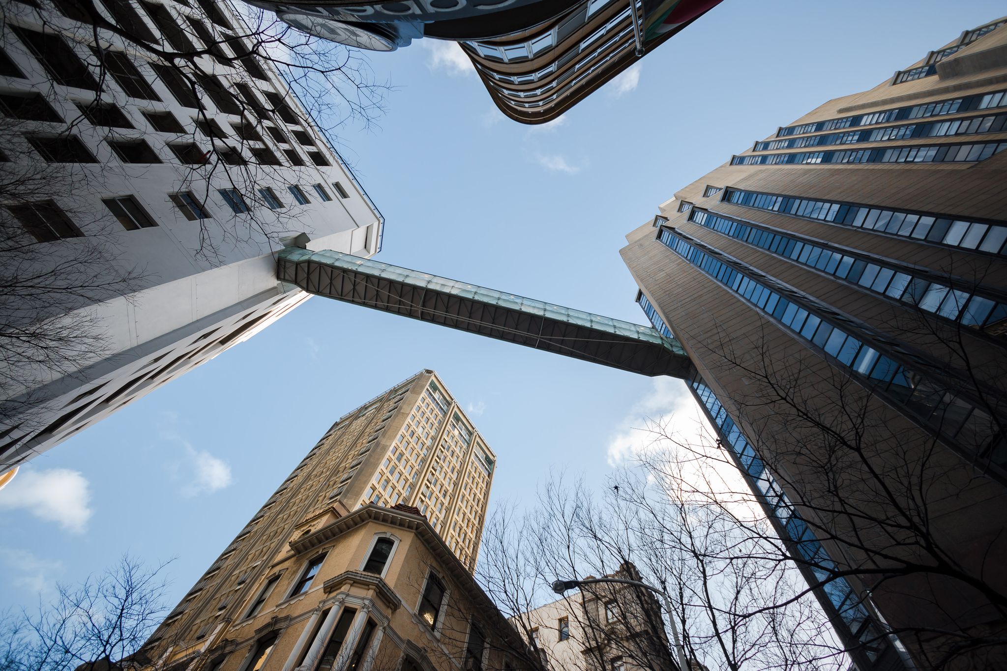 Looking up between city skyscrapers joined by a skybridge