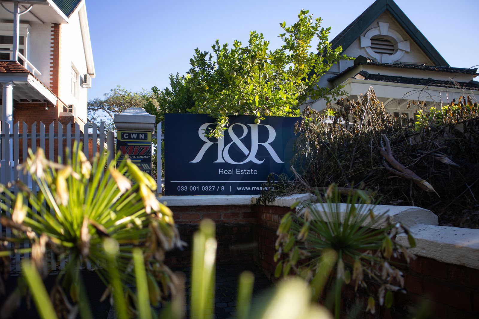 A business sign at the entrance to a property, framed by garden plants